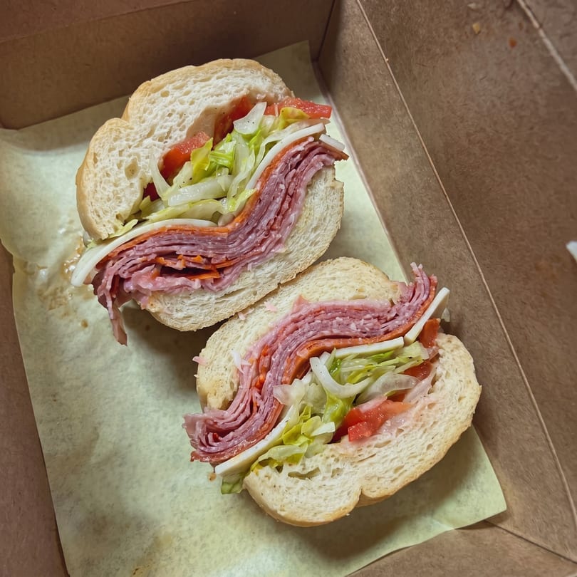 A large deli sub sandwich, cut in half, with various meats, cheese, lettuce, and tomatoes.