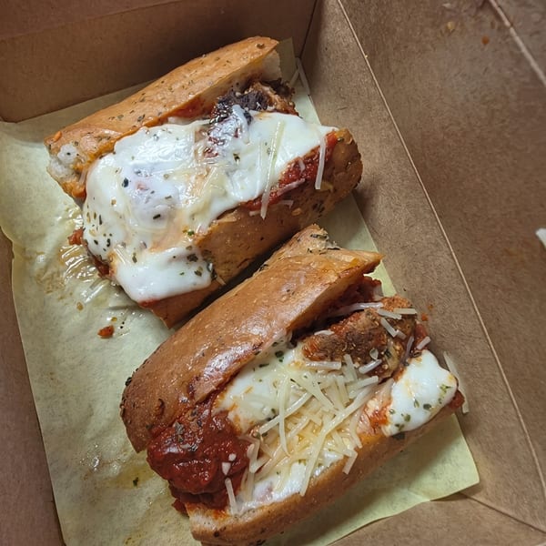 Two meatball subs with melted cheese and marinara sauce in a cardboard box.