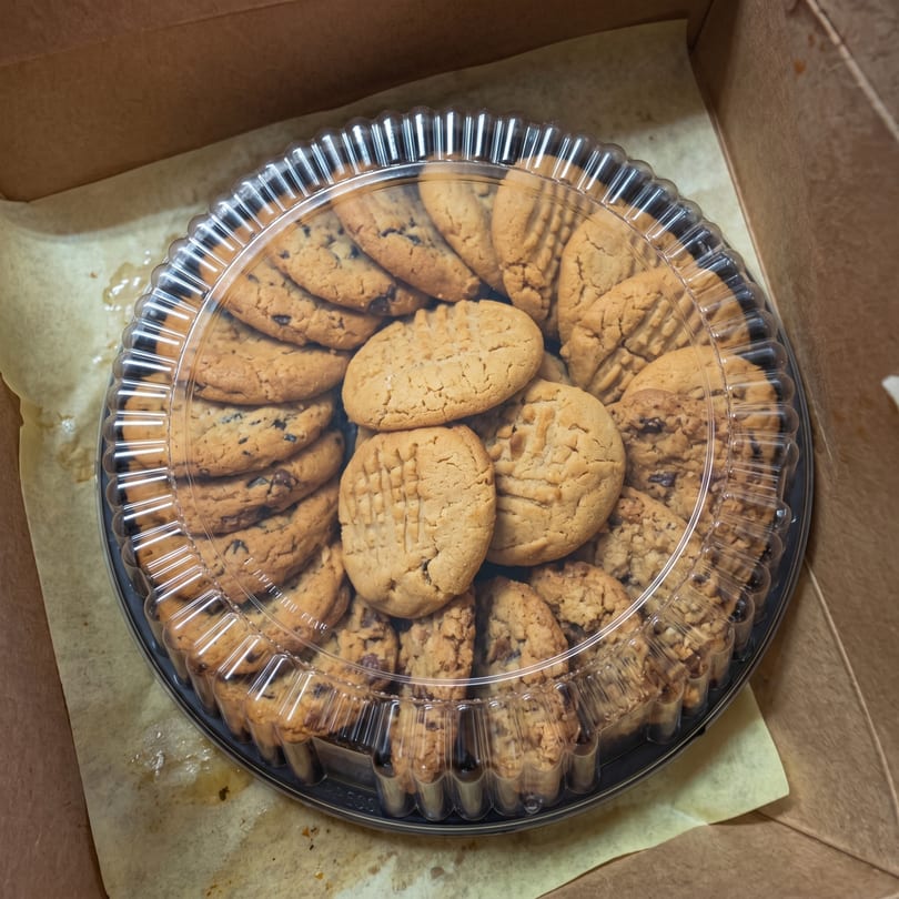 A plastic tray of chocolate chip and peanut butter cookies sits inside a cardboard box.