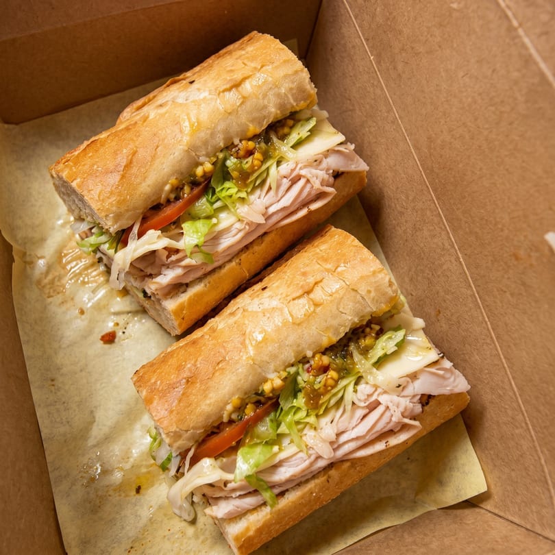 Two turkey sandwiches with lettuce, tomato, and relish in a brown takeout box.